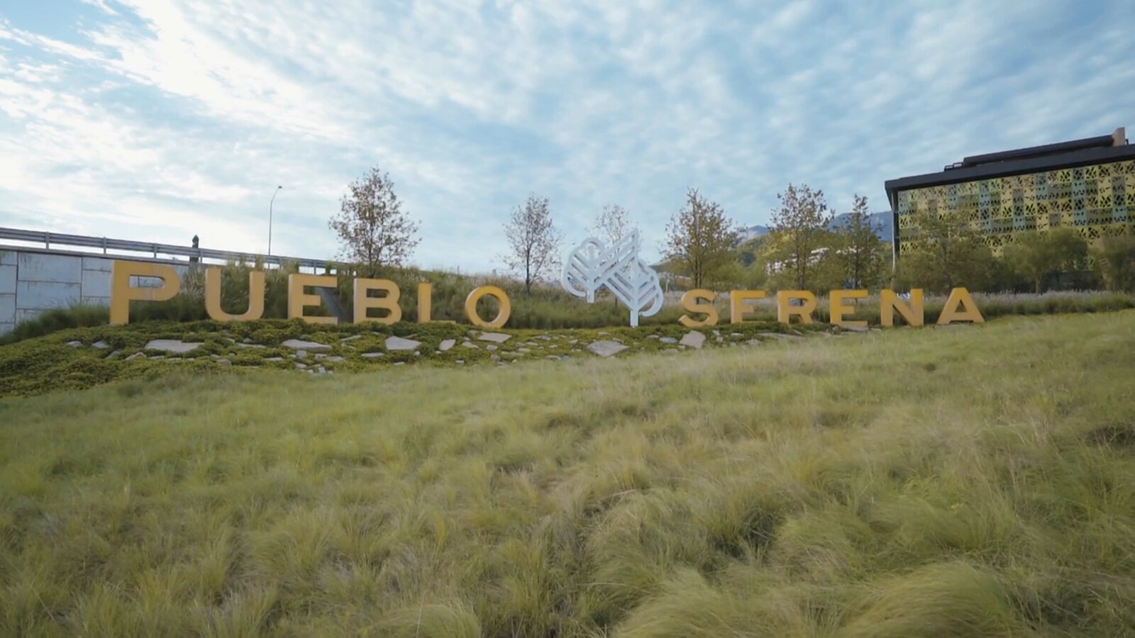 Letras de Pueblo Serena sobre pasto alto, en el acceso desde Carretera Nacional