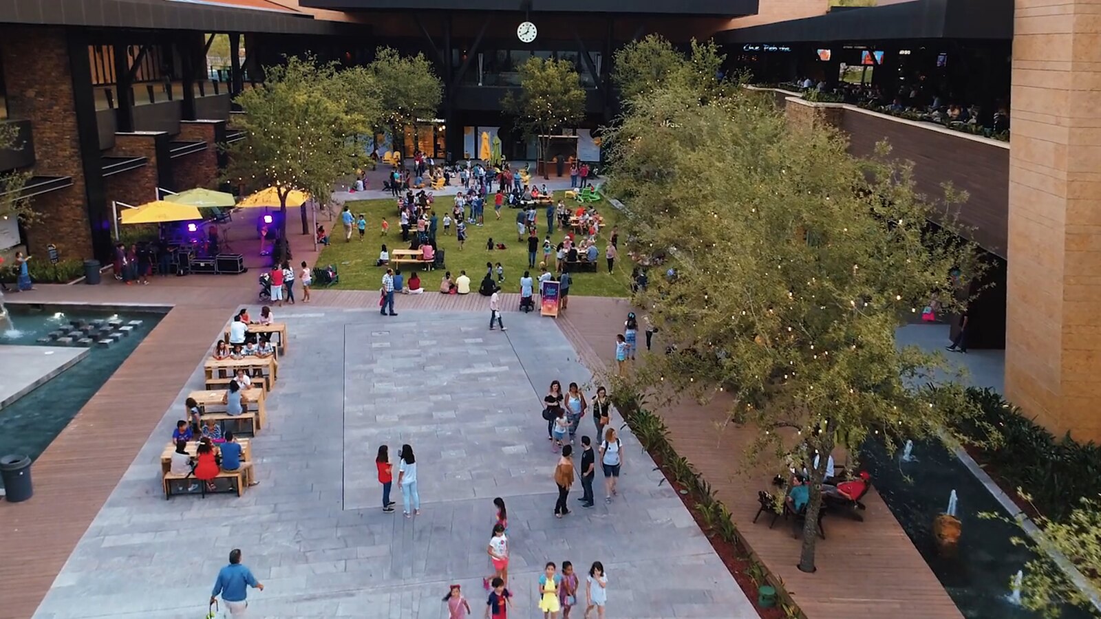 Plaza central de Pueblo Serena con mesas, árboles y gente caminando